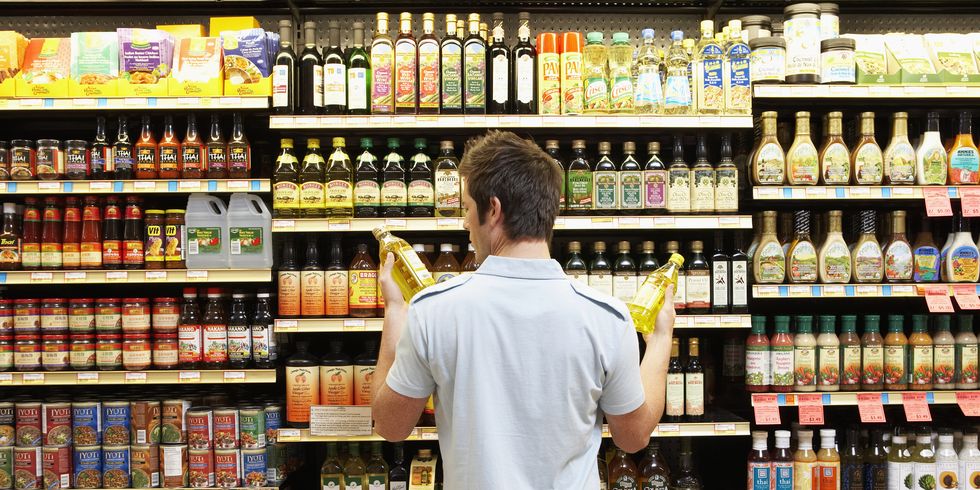 young man in supermarket comparing bottles of oil, rear view, close up