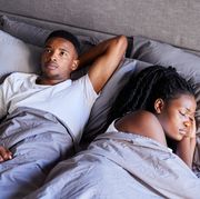 young man looking unhappy while lying in bed with his sleeping wife