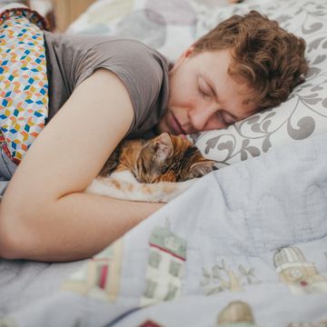 young man lying in the bed with the tabby cat sleeping