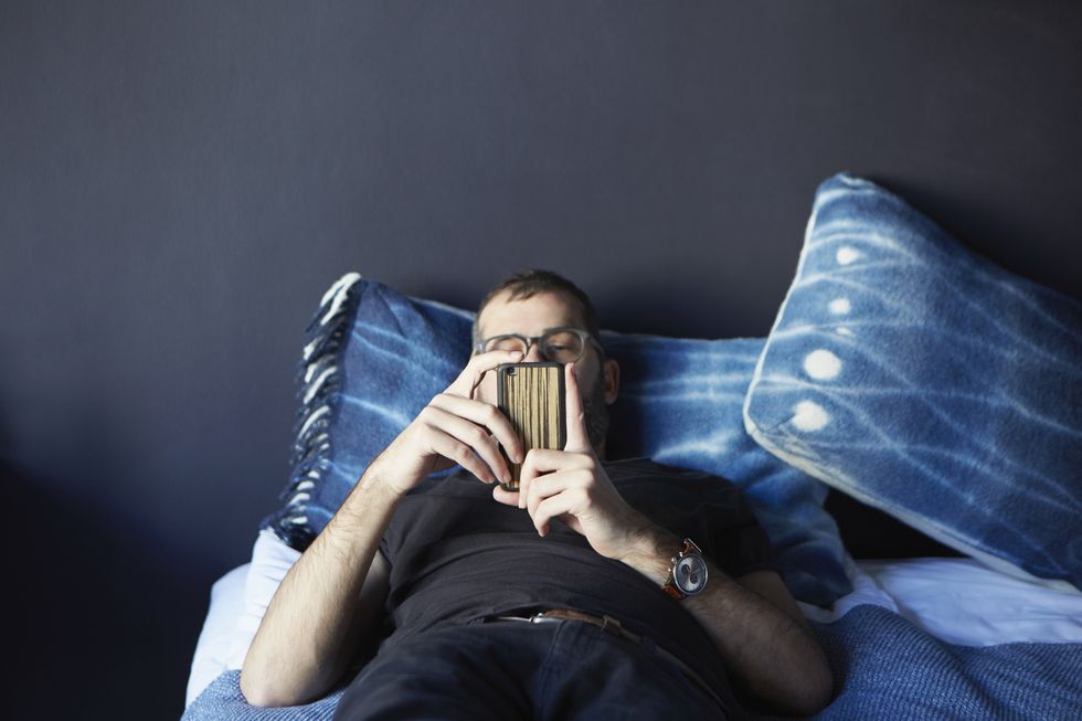 Young man lying on bed looking at smartphone
