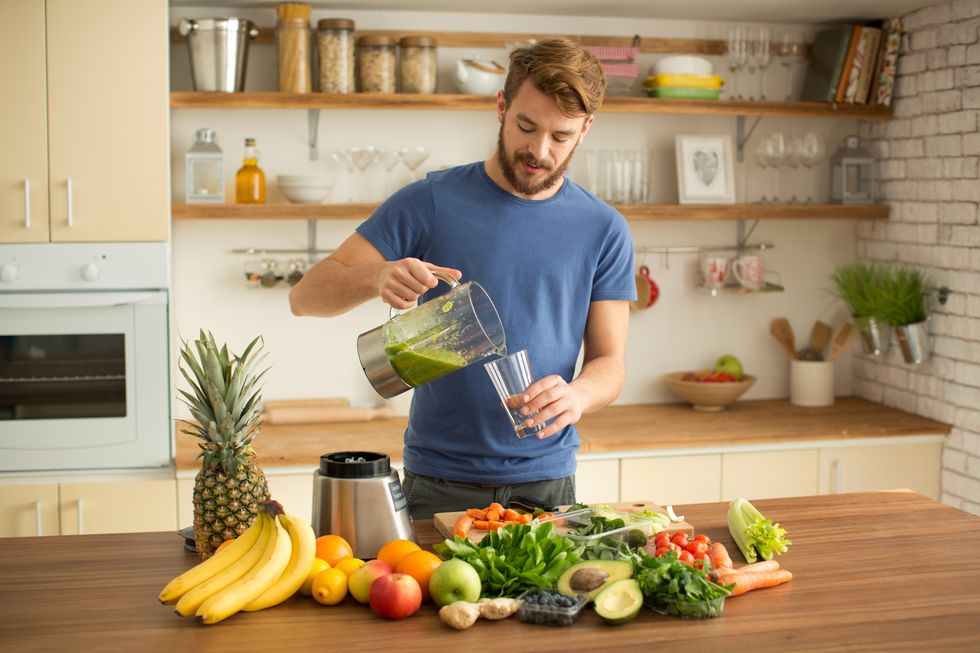 Young man making juice or smoothie in kitchen.