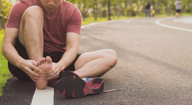 young man massaging his painful foot from jogging and running on track