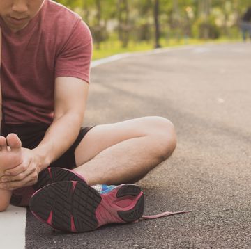 young man massaging his painful foot from jogging and running on track