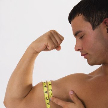young man measuring biceps, using tape measure