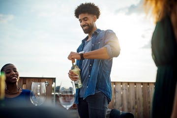 young man opening wine bottle at rooftop party