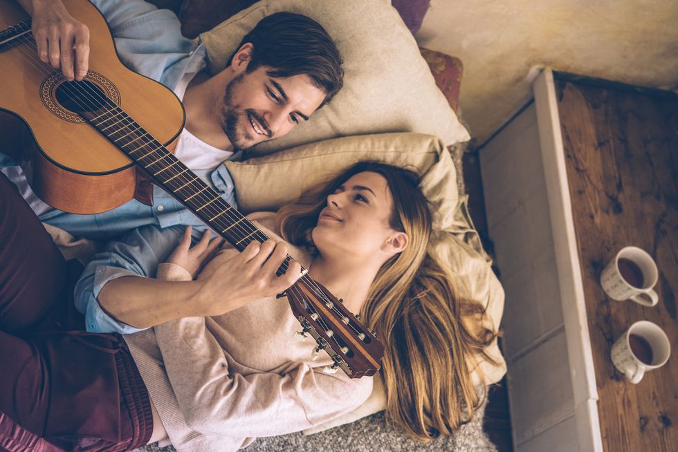 young man plays guitar for young woman on sofa