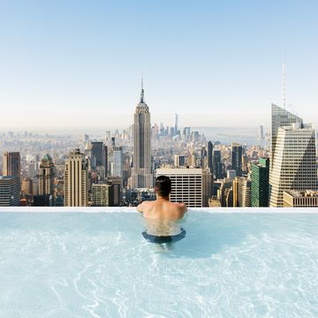 Young man relaxing in a swimming pool with view towards New York City skyline