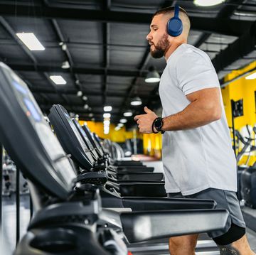 young man running on the treadmill while listening to music in the gym
