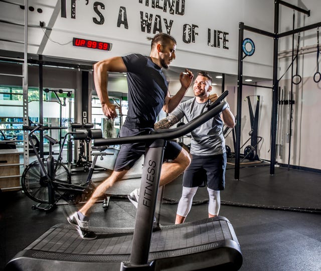 young man running on treadmill while fitness instructor motivates him