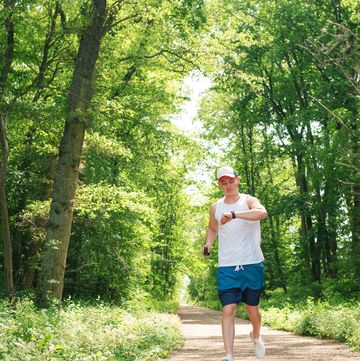 a young man runs in the park. body control during sports with the help of technology. smart watch. telephone. sports app. training. energy.
