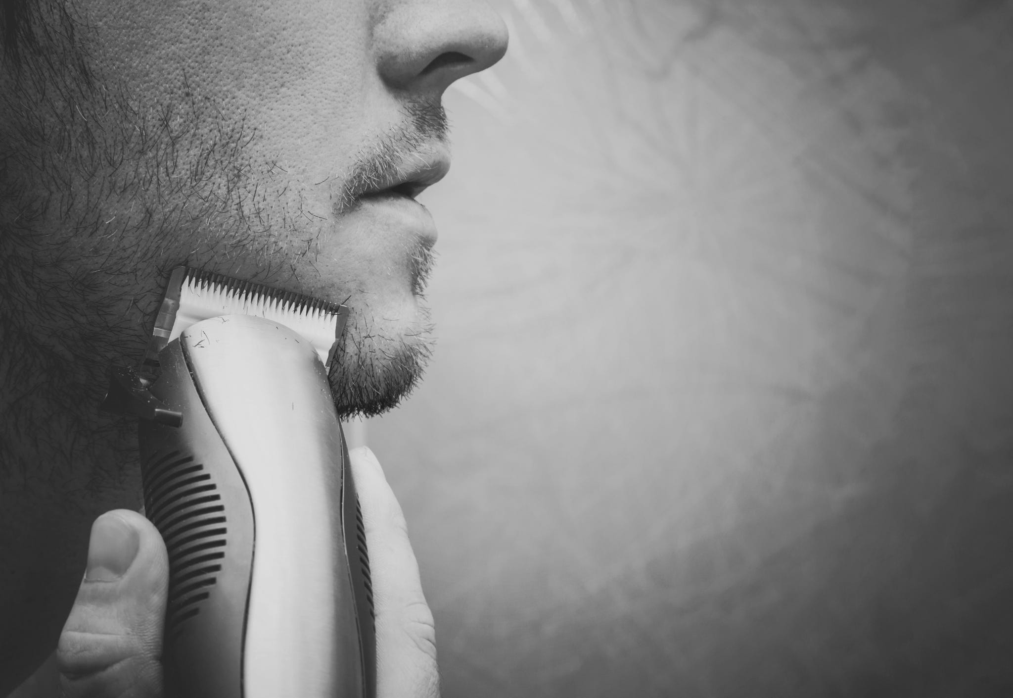 Young man shaving with electric razor.