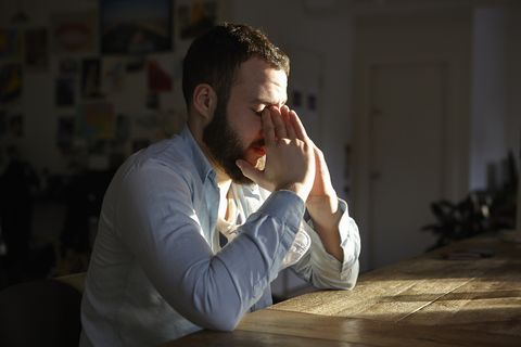 Young man sitting at kitchen table with hands on face