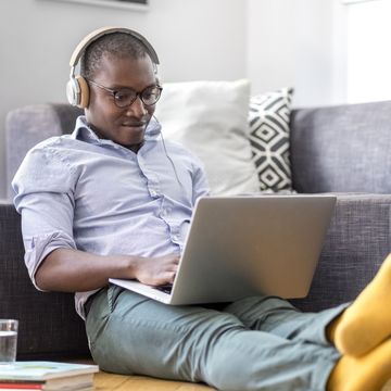 young man sitting on the floor in the living room using laptop and headphones