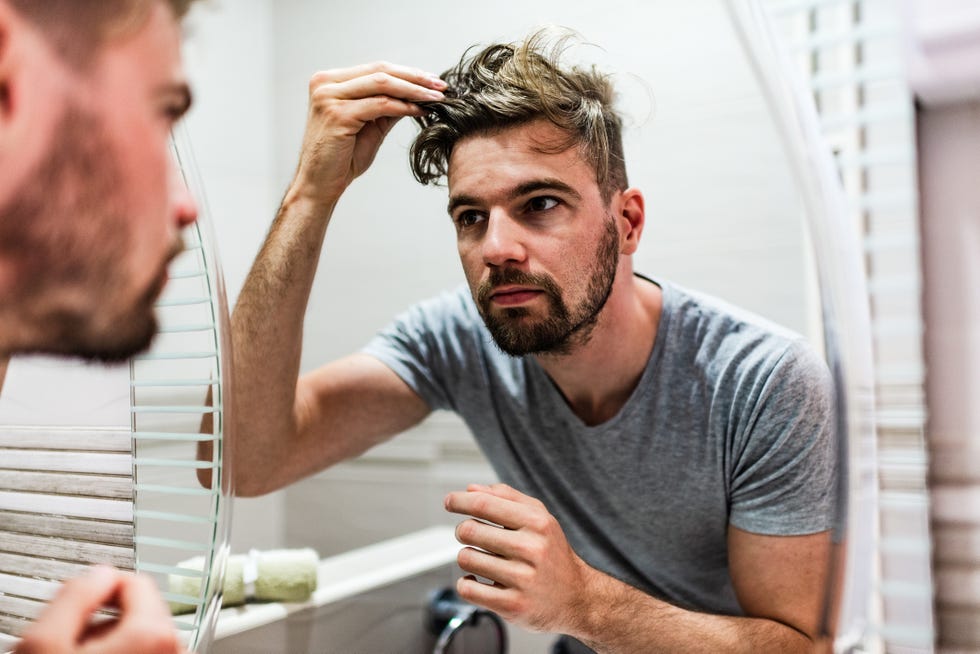 hombre que se mira el pelo en el espejo del lavabo