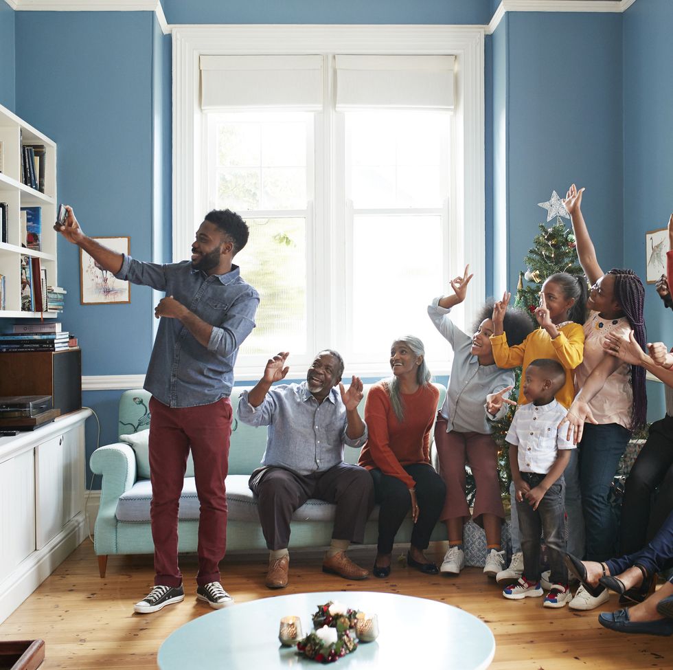 a young black man taking a selfie in a living room surrounded by family and friends