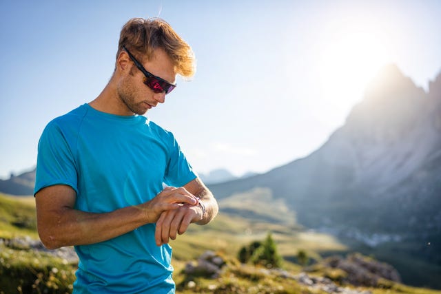 young man trail running on the mountain, looking sport watch