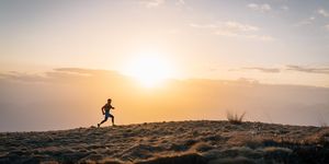 young man trail runs up mountain at sunrise
