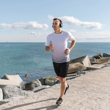 young man wearing wireless headphones jogging on pier near sea