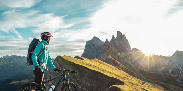 young man with mountain bike on seceda mountain peak at sunrise. puez odle, trentino, dolomites, italy.