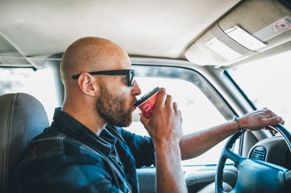 daylight saving sleep - YYoung man with sunglasses and beard on a road trip with takeaway drink