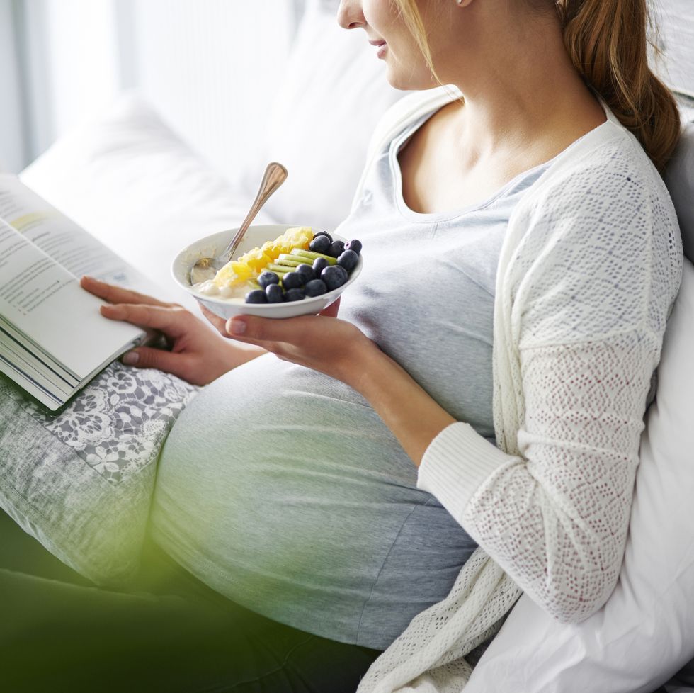 Young mother eating and reading book at home. Debica, Poland