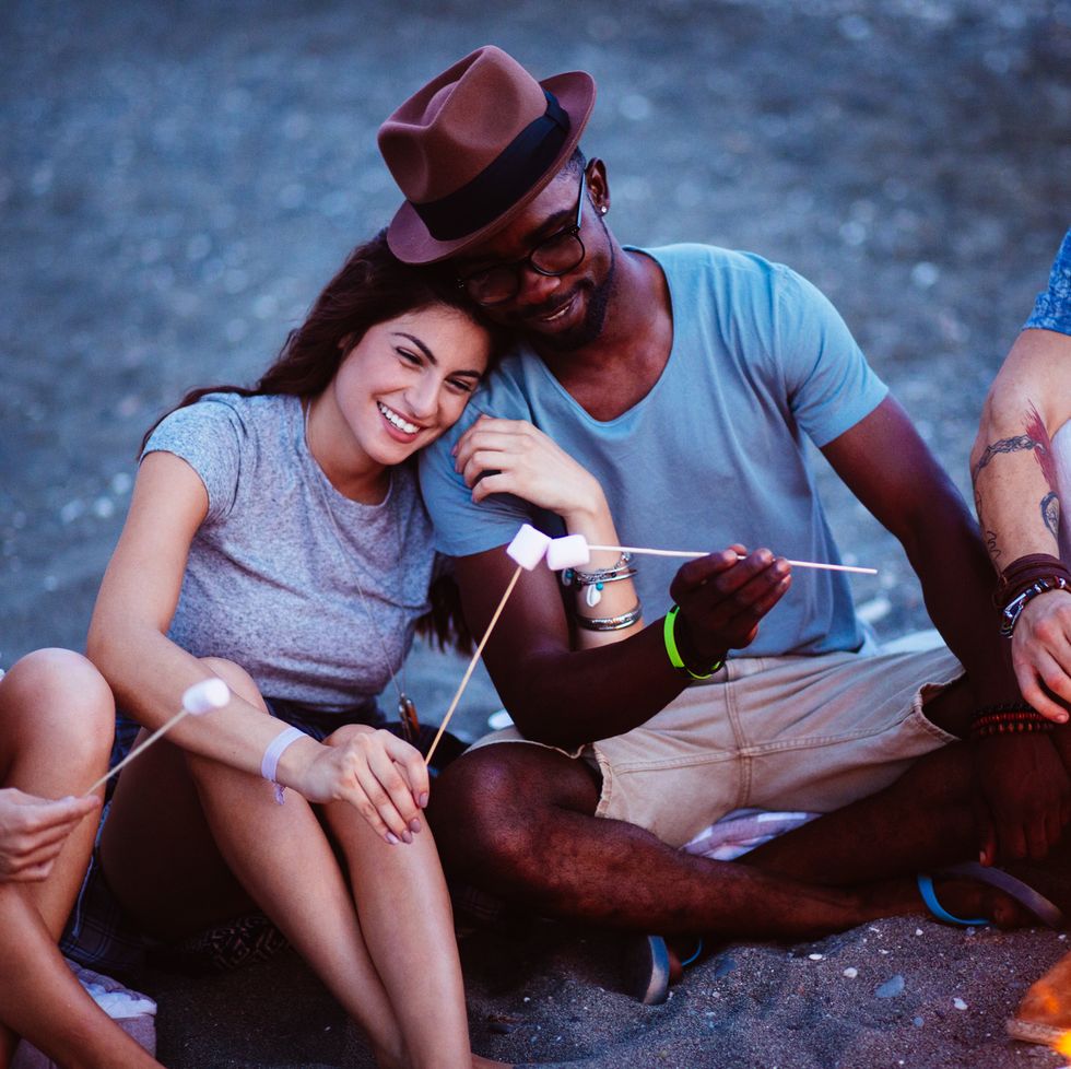 young couple preparing smores on the beach with friends