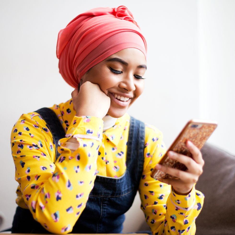 young muslim woman laughing while using mobile phone
