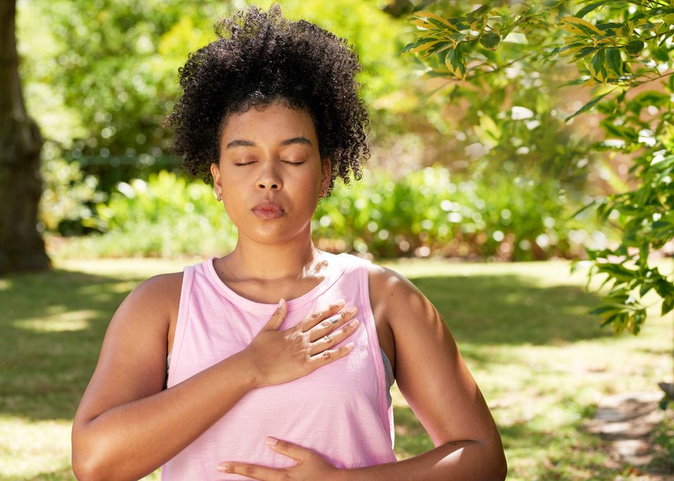 young mutli ethnic woman practices deep belly breathing, meditation in park