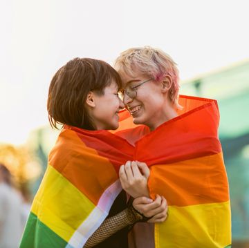 young non binary couple in love hugging under a rainbow flag
