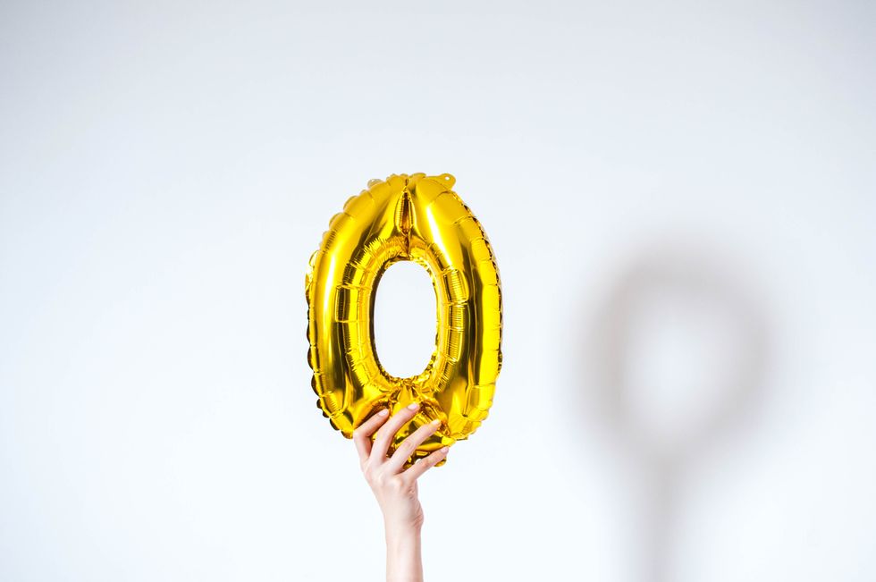 A young person is holding a golden-colored number zero on a white background