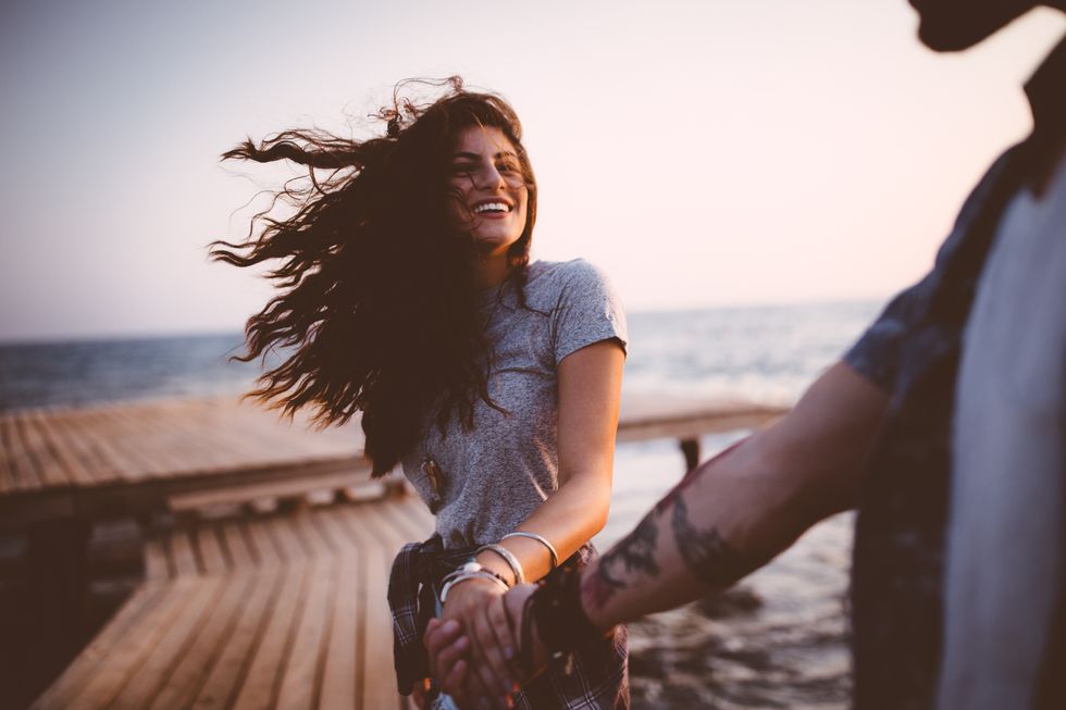 young playful hipster couple holding hands on jetty at sunset