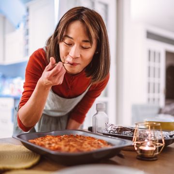 young pretty asian woman tasting a dish of pasta she prepared while serving food on the table at home