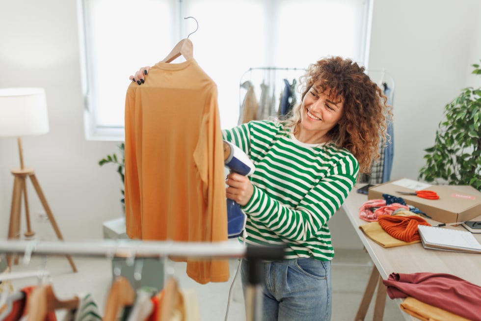 a woman using a clothes steamer on an orange top