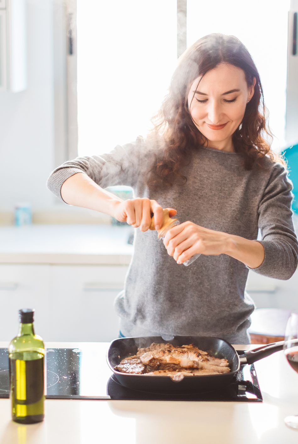 young smiling woman cooking in the kitchen, adding pepper to the grilled meat healthy food concept