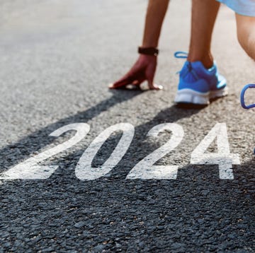 young sports man preparing to run with new year number 2024 on asphalt road