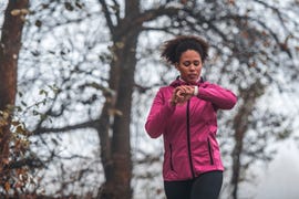 young sportswoman running and checking pulse on smart watch on foggy morning