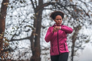 young sportswoman running and checking pulse on smart watch on foggy morning