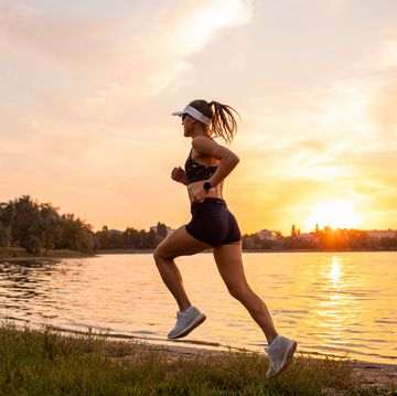 young sportswoman running at sunset by lakeside