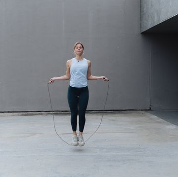 young sportswoman skipping rope while standing against wall