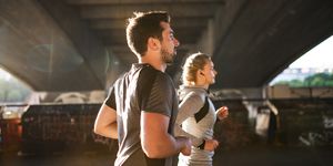 young sporty man and woman with earphones running under the bridge outside in a city