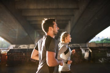 young sporty man and woman with earphones running under the bridge outside in a city