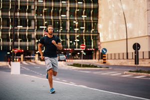 young sporty man jogging through city streets with backpack on back