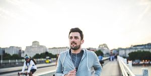 Young sporty man with earphones running on the bridge outside in a city.