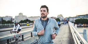 Young sporty man with earphones running on the bridge outside in a city.