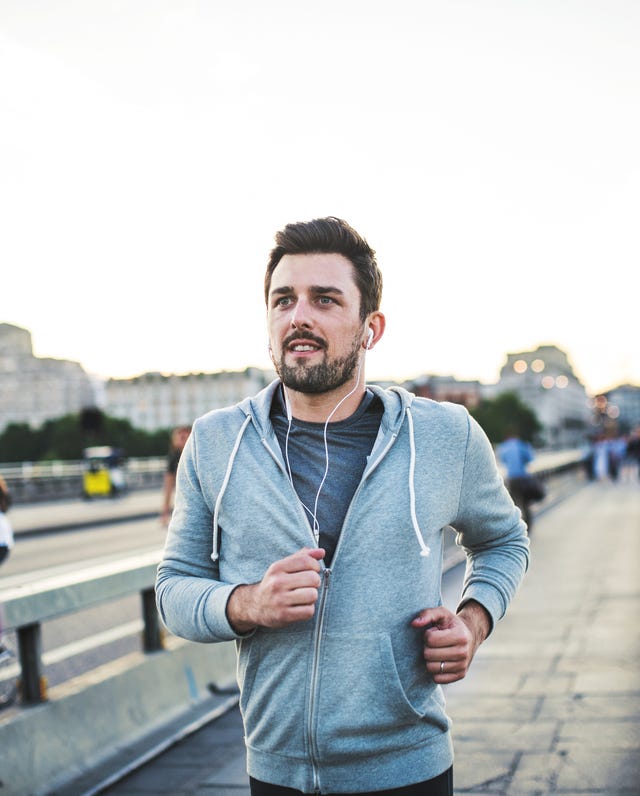 Young sporty man with earphones running on the bridge outside in a city.