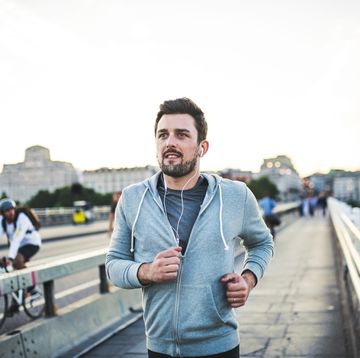 Young sporty man with earphones running on the bridge outside in a city.