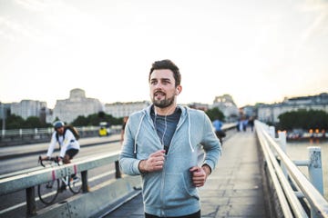 young sporty man with earphones running on the bridge outside in a city