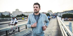young sporty man with earphones running on the bridge outside in a city