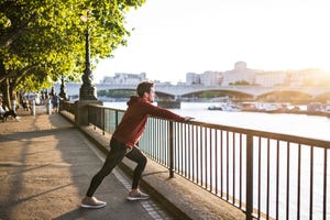 young sporty man with earphones stretching on a railing outside in a london city