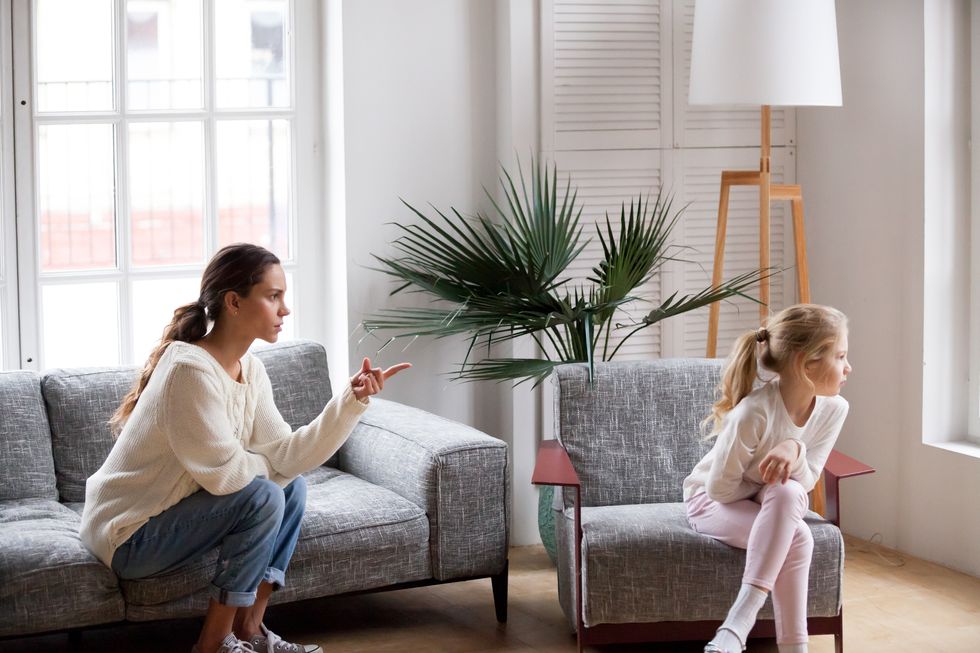 Young strict mother scolding stubborn sulky daughter in living room